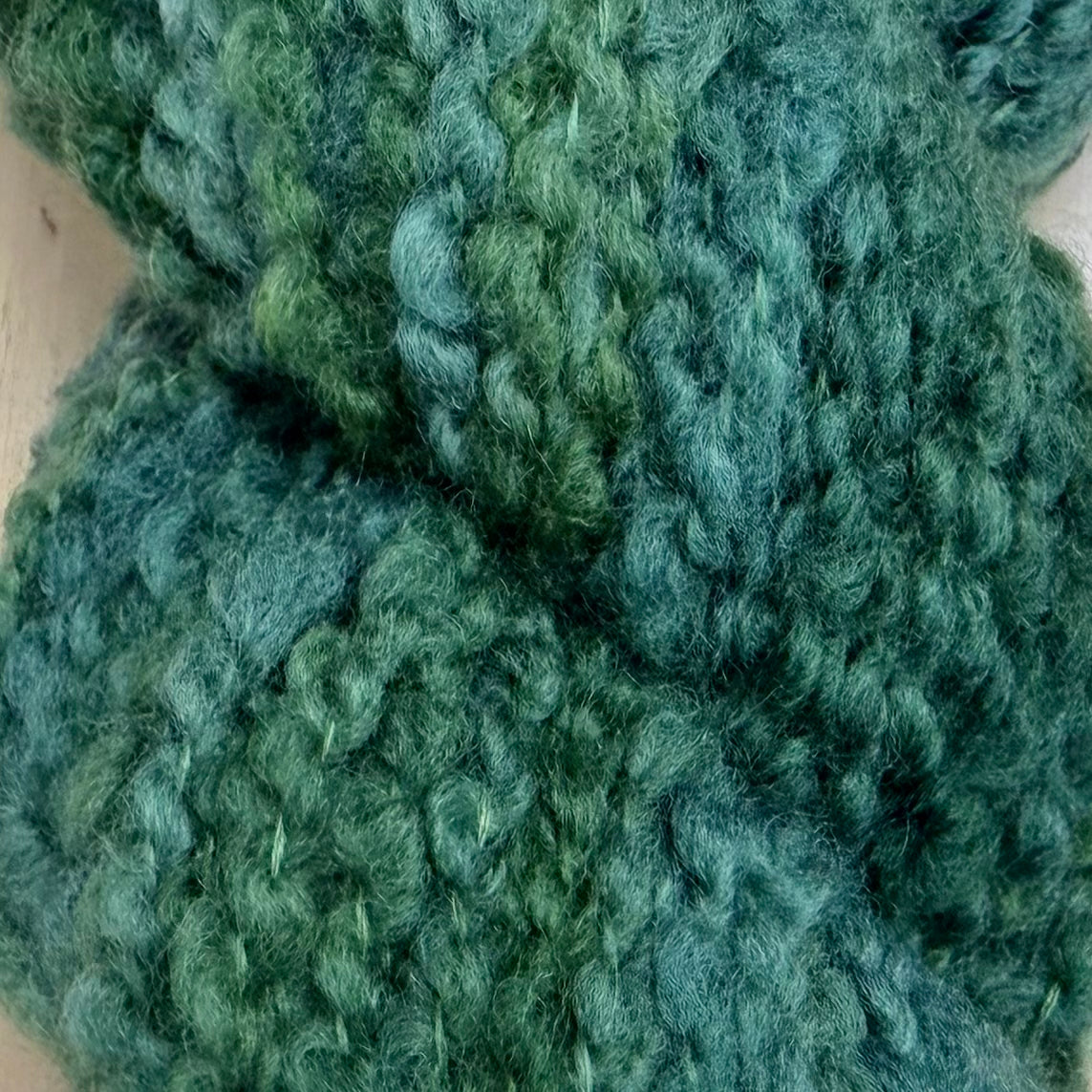 Hokuto by Apple Fiber Studio - Close-up of chunky knitted yarn in a variegated green and teal colorway, showing the thick, fuzzy texture of the wool.