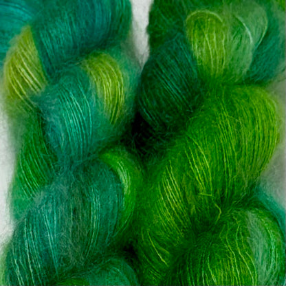 Delicious by Apple Fiber Studio. Close-up of two skeins of fuzzy yarn in shades of green and teal, showing the soft texture and variegated color from bright lime green to deep emerald and teal.