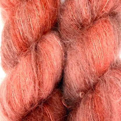 Close-up of soft, fuzzy yarn or fiber skeins in a warm dusty coral-pink color against a white background. Hand-dyed Cortland by Apple Fiber Studio in Alpaca and Silk at Apple Yarns.