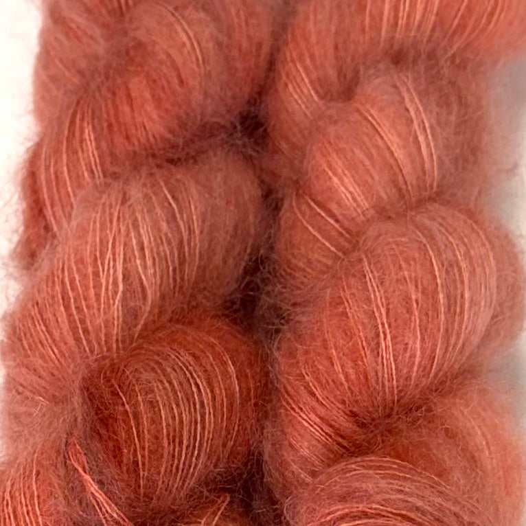 Delicious by Apple Fiber Studio. Close-up of soft, fuzzy yarn skeins in a warm dusty rose or terracotta pink color against a light neutral background.