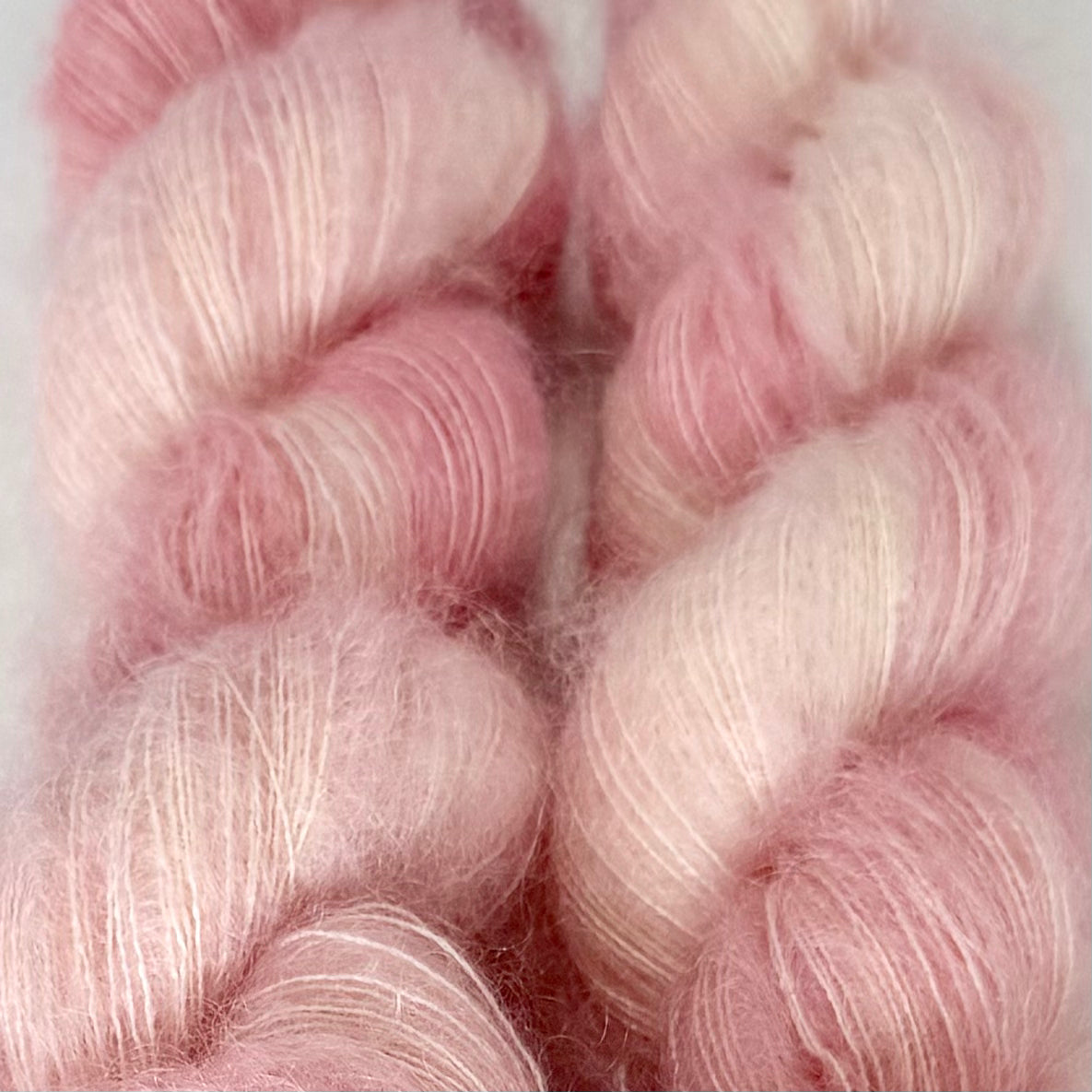 Delicious by Apple Fiber Studio. Two soft, fuzzy yarn skeins in a blended pastel pink and off-white colorway, shown in a close-up texture shot.