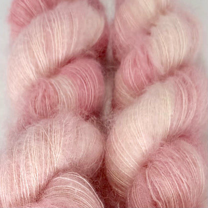 Delicious by Apple Fiber Studio. Two soft, fuzzy yarn skeins in a blended pastel pink and off-white colorway, shown in a close-up texture shot.
