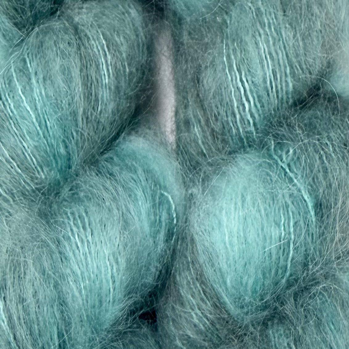 A close-up of fluffy, soft yarn or fiber skeins in a pale aqua or mint teal color, filling the entire frame. Hand-dyed Cortland by Apple Fiber Studio in Alpaca and Silk at Apple Yarns.