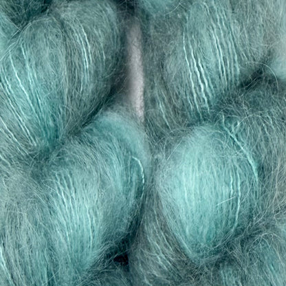 A close-up of fluffy, soft yarn or fiber skeins in a pale aqua or mint teal color, filling the entire frame. Hand-dyed Cortland by Apple Fiber Studio in Alpaca and Silk at Apple Yarns.