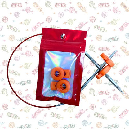 Point Protectors: A red resealable pouch containing three orange circular knitting needle tips, with two silver knitting needles visible behind the pouch on a white patterned background.