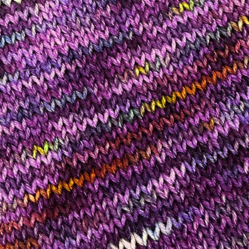 YarnFall 2026 Spiced Plum Hand-Dyed Yarn - Sock & Worsted, Close-up of a knitted textile with a variegated purple pattern, featuring diagonal stripes of orange, yellow, green, and white yarn.