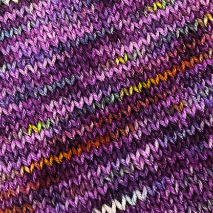 YarnFall 2026 Spiced Plum Hand-Dyed Yarn - Sock & Worsted, Close-up of a knitted textile with a variegated purple pattern, featuring diagonal stripes of orange, yellow, green, and white yarn.