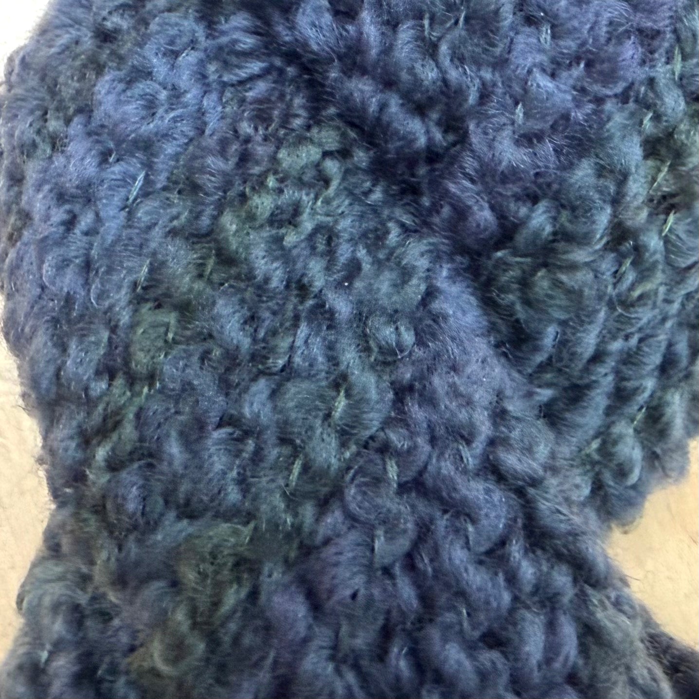 Hokuto by Apple Fiber Studio - A close-up of chunky, curly knit yarn in a variegated colorway transitioning from slate blue to dark teal and charcoal gray.