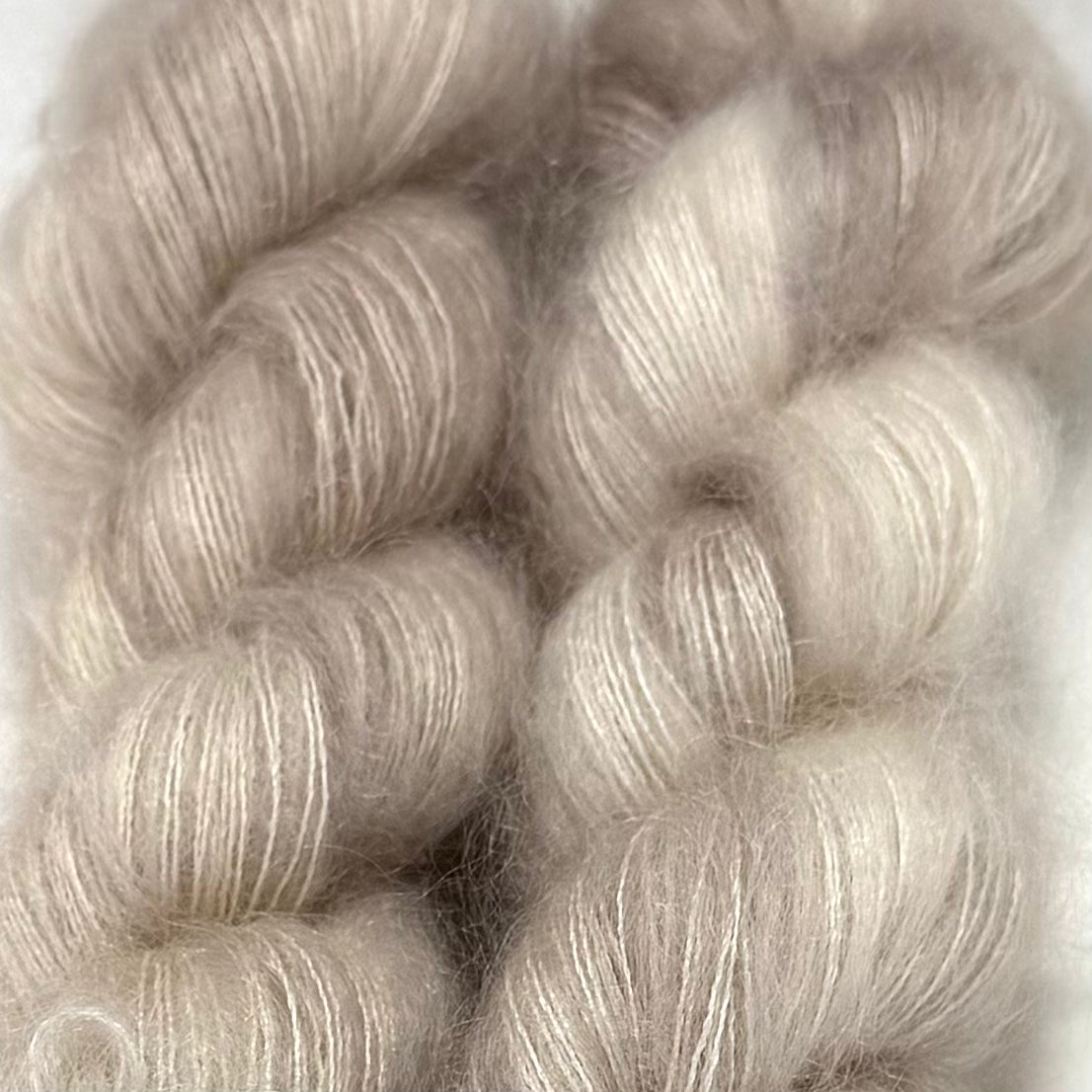 Delicious by Apple Fiber Studio. Close-up of soft, fluffy yarn skeins in a pale warm gray-beige tone against a light neutral background.
