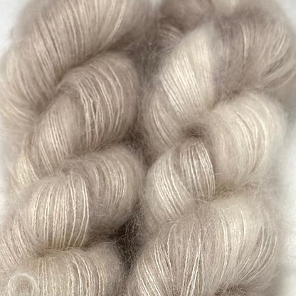 Delicious by Apple Fiber Studio. Close-up of soft, fluffy yarn skeins in a pale warm gray-beige tone against a light neutral background.