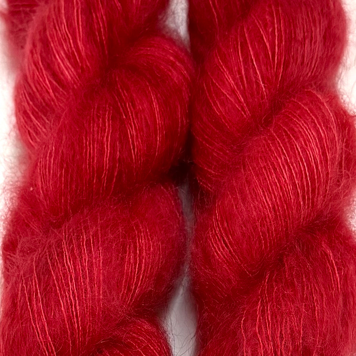 Delicious by Apple Fiber Studio. Two twisted skeins of fluffy yarn in a rich, deep red color, shown in a close-up shot against a white background.