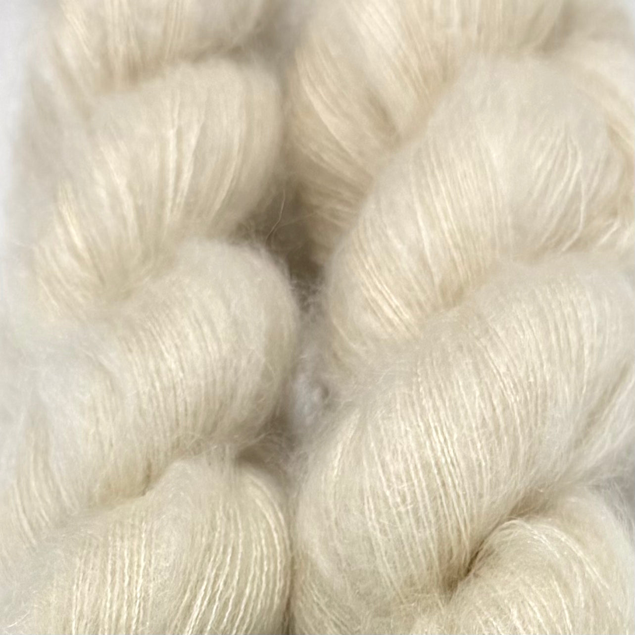 Delicious by Apple Fiber Studio. Close-up of soft, fluffy cream-colored yarn skeins filling the frame, showing the texture and color of the fiber.