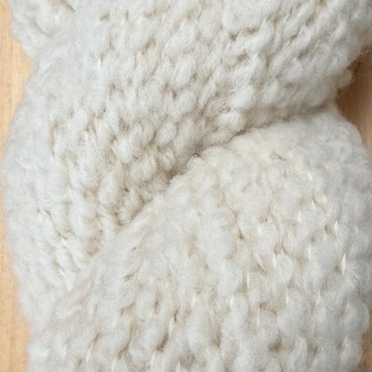 Hokuto by Apple Fiber Studio - A close-up of chunky, thick-knit cream or off-white yarn, showing its soft, fuzzy texture against a light wood background.