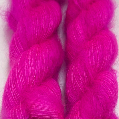 Delicious by Apple Fiber Studio. Two bright fuchsia pink skeins of fluffy yarn filling the frame against a pale background.