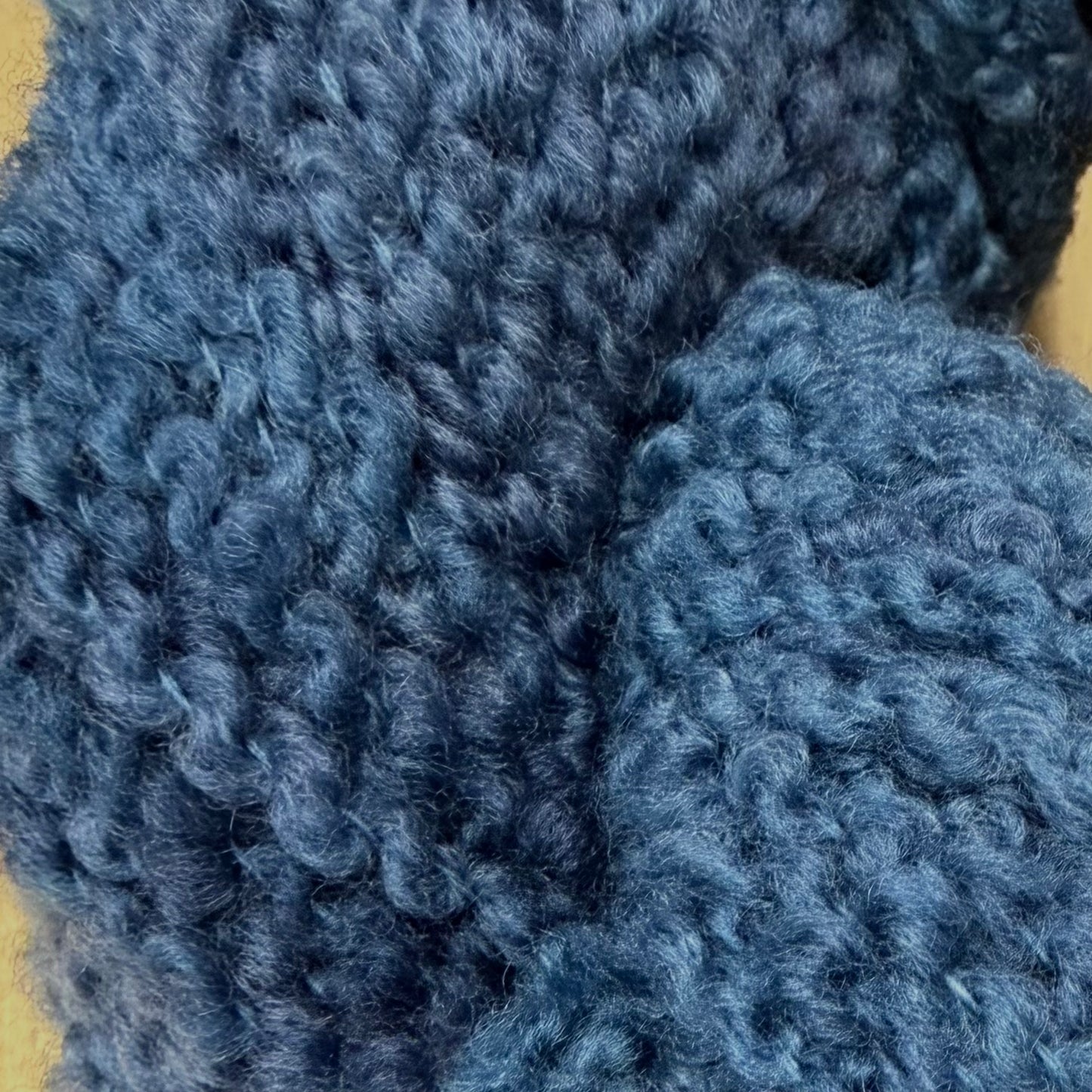 Hokuto by Apple Fiber Studio - A close-up of chunky, curly knit fabric in a dusty medium blue color, showing the detailed texture of the yarn.