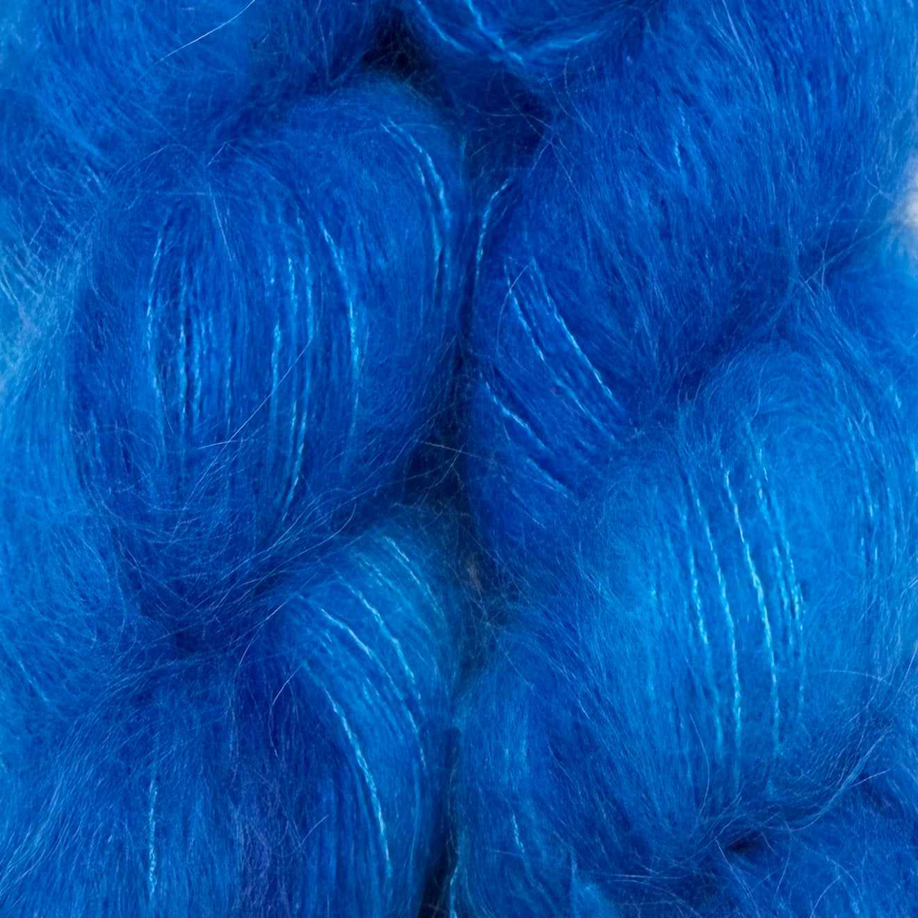 A close-up of bright royal blue fluffy fiber, likely yarn or felt, filling the entire frame. Hand-dyed Cortland by Apple Fiber Studio in Alpaca and Silk at Apple Yarns.