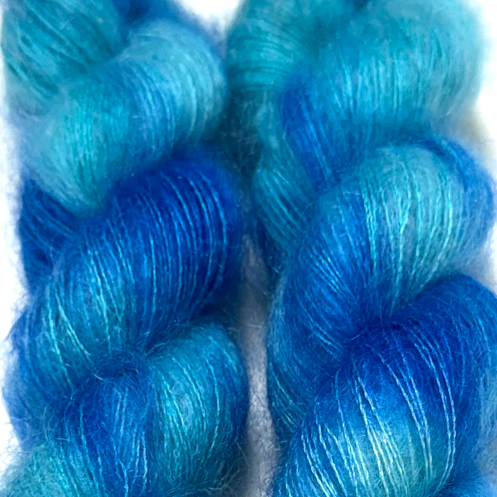 Delicious by Apple Fiber Studio. Two twisted hanks of fluffy yarn in a variegated blue and turquoise colorway, photographed close-up against a white background.