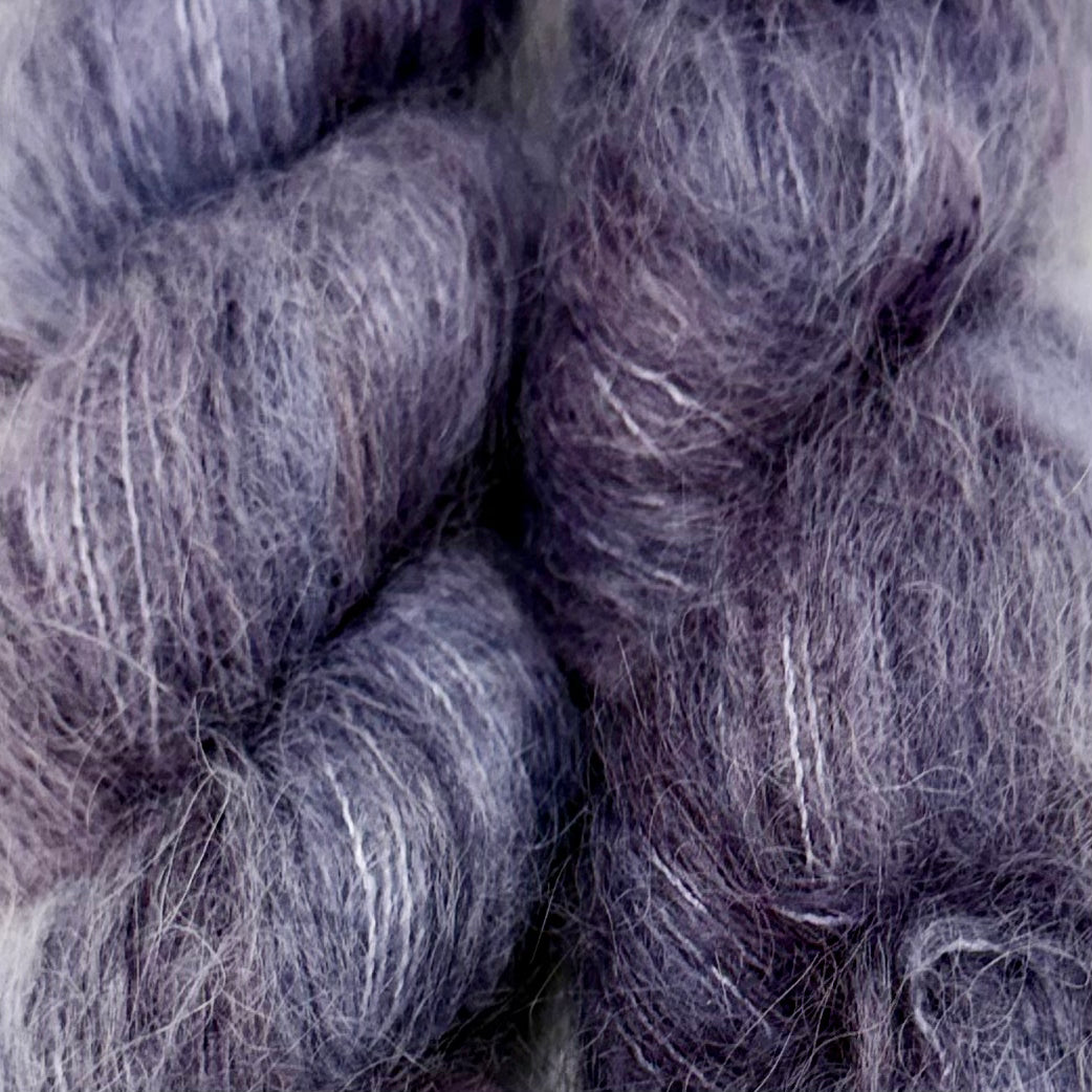 Close-up of soft, fuzzy yarn or fiber skeins in a muted lavender-gray color with subtle white and darker gray variation. Hand-dyed Cortland by Apple Fiber Studio in Alpaca and Silk at Apple Yarns.